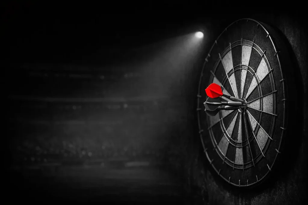 Darts betting: a dartboard under a spotlight with three darts, one with a red flight